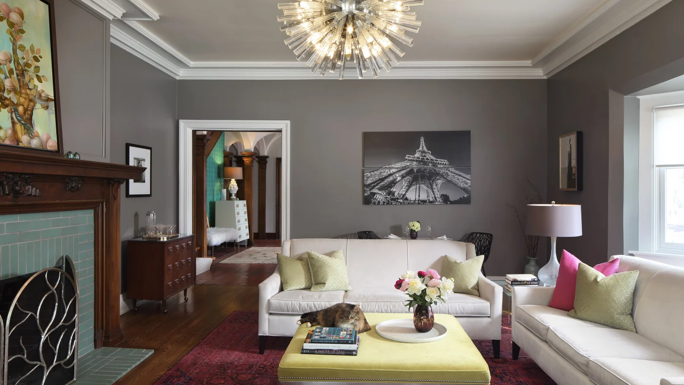 A beautiful living room in a Shorewood home with newly painted gray walls, white trim, a fireplace and mantle, art, antique furniture, and a lovely white couch and loveseat.