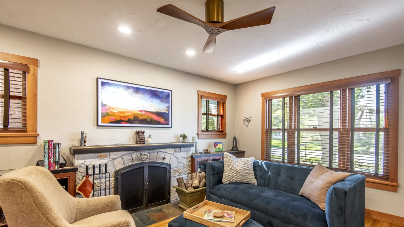 A cozy, beautifully furnished living room in a Washington County home with a fireplace, mantle with a watercolor painting above, brown lounging chairs, a darker bluish couch, and newly painted tan walls and ceilings.