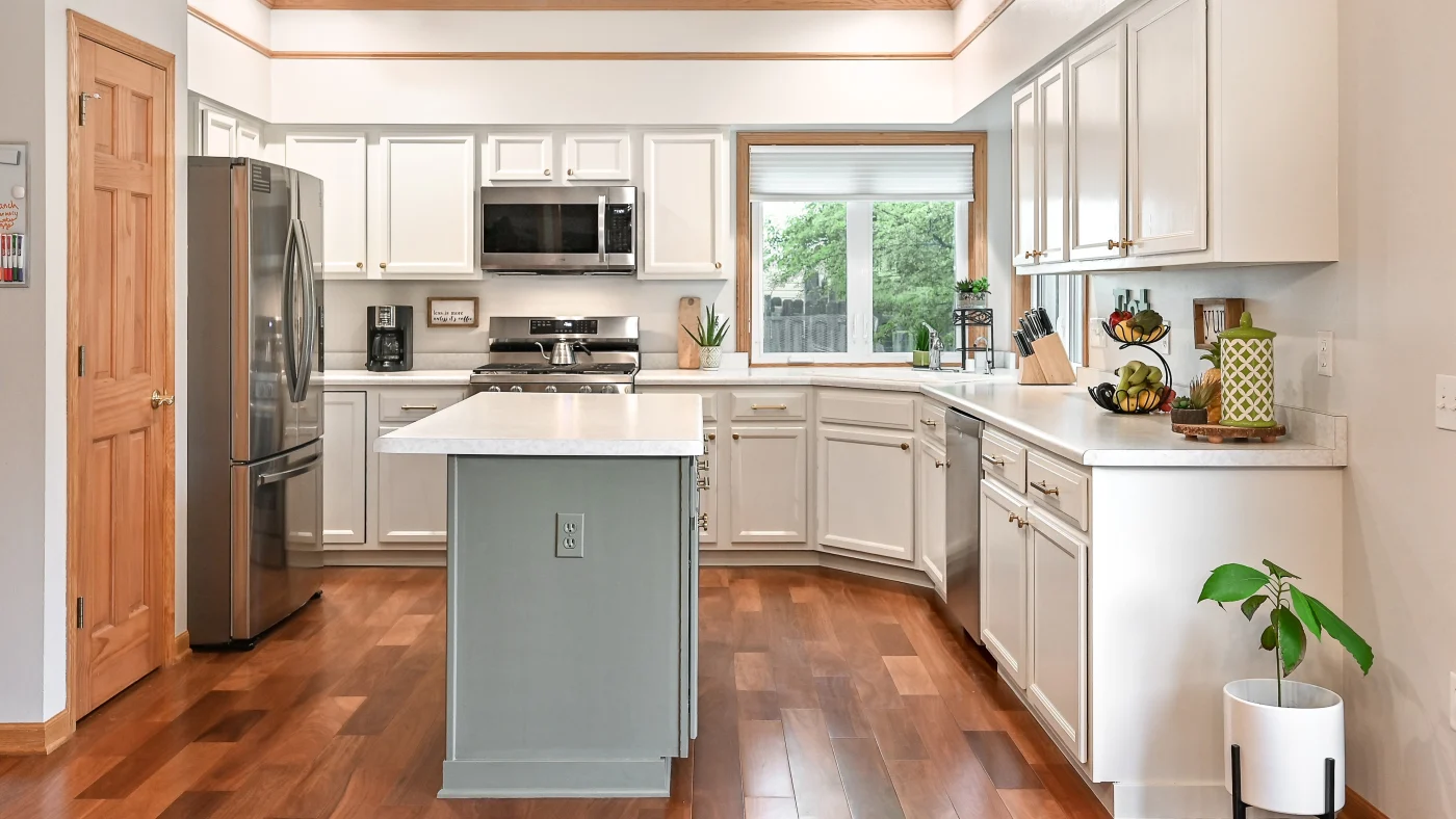 The Madson family kitchen in their Saukville home with newly painted schoolhouse white cabinets, lovely white countertops, and wood flooring.