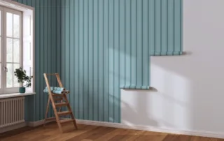 A remodeled room with a new white window enclosure on the left and striped wallpaper installed on the wall on the right, with a ladder and rolls of wallpaper in the corner.