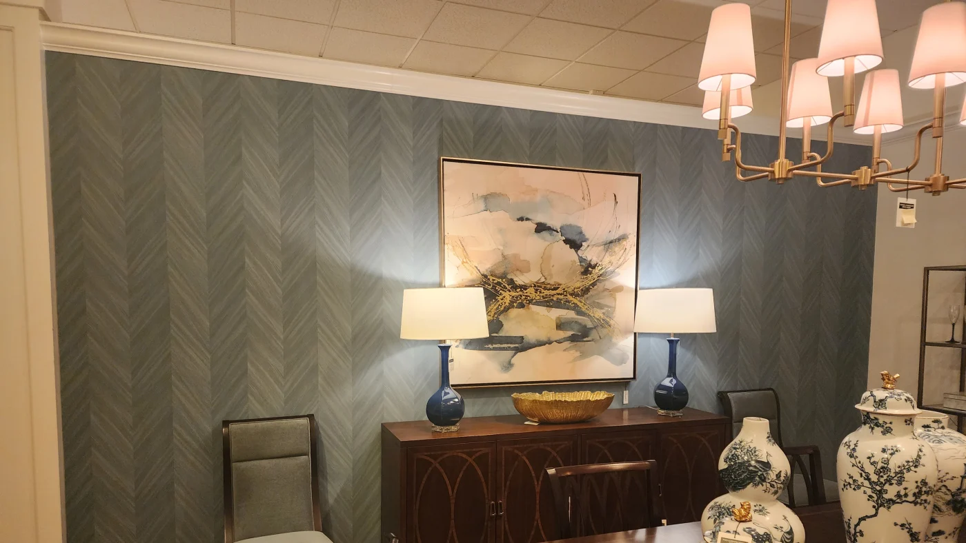 A beautifully furnished showroom with an antique table, lamps, and Chinese cases, with a newly painted light blue wall and painted white trim.