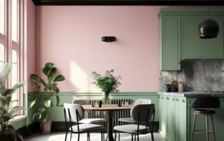 A modern dining area next to a kitchen with potted plants in the corner, a small round wood table and chairs, and newly painted tan walls to match kitchen cabinets and black trim.